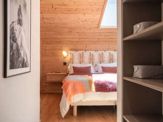 Experience cozy mountain living in this charming bedroom featuring warm wood paneling and a comfortable bed adorned with a vibrant, textured throw.