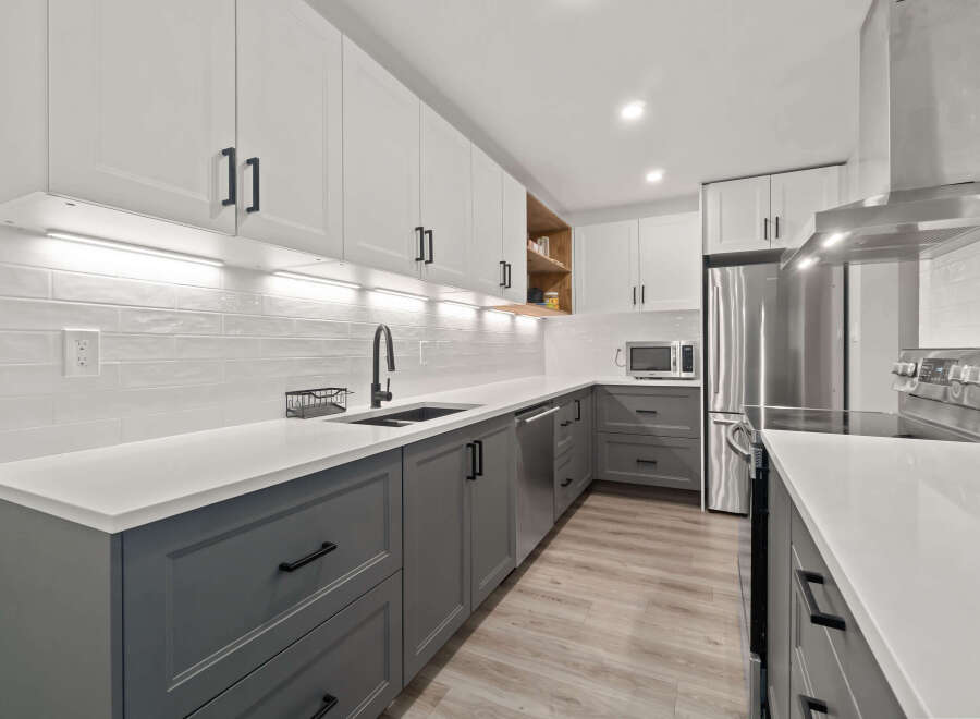 This modern kitchen boasts sleek white cabinetry paired with stylish gray lower cabinets, creating a sophisticated and inviting atmosphere.