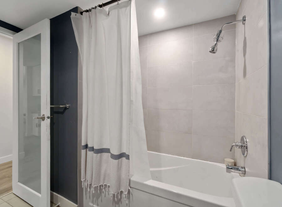 Step into this modern bathroom featuring a sleek shower and a pristine white bathtub.