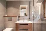 This modern bathroom features a stylish wooden vanity with a sleek white sink, complemented by a large mirror with integrated lighting.