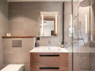 This modern bathroom features a stylish wooden vanity with a sleek white sink, complemented by a large mirror with integrated lighting.