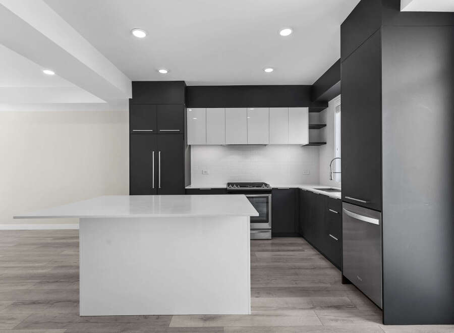 This modern kitchen boasts sleek, dark cabinetry complemented by bright white countertops and a spacious island, perfect for meal preparation and entertaining.