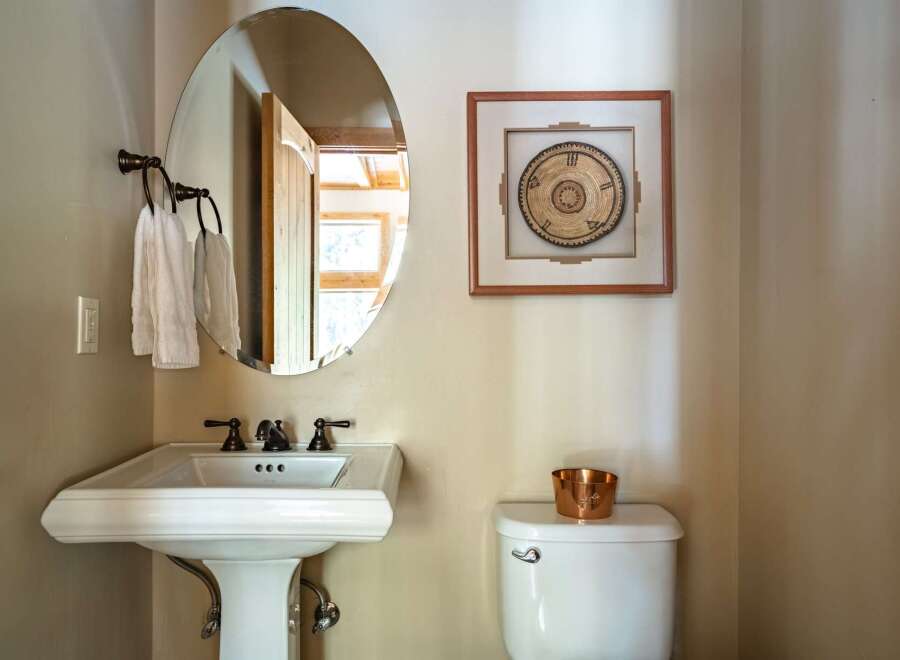 This charming bathroom features a stylish pedestal sink, a sleek oval mirror, and a decorative wall hanging, creating a blend of functionality and aesthetics.