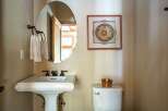 This charming bathroom features a stylish pedestal sink, a sleek oval mirror, and a decorative wall hanging, creating a blend of functionality and aesthetics.