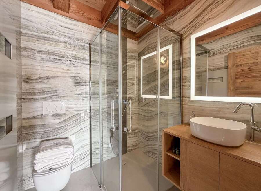 Step into luxury with this stunning bathroom featuring a modern glass shower, elegant marble-effect walls, and a sleek floating vanity.