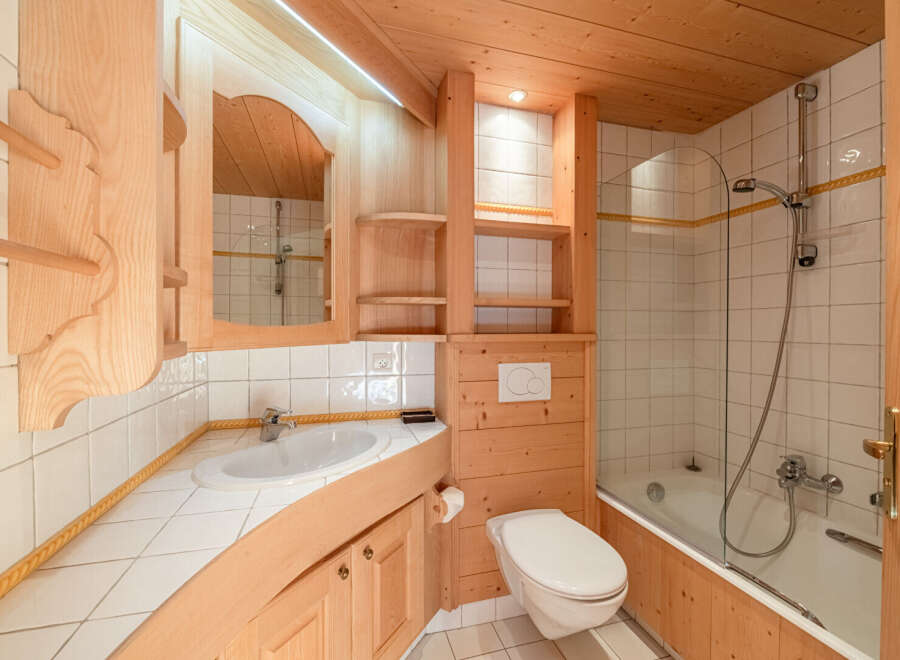 This charming bathroom features a warm, inviting ambiance with its wooden accents and bright white tiles.