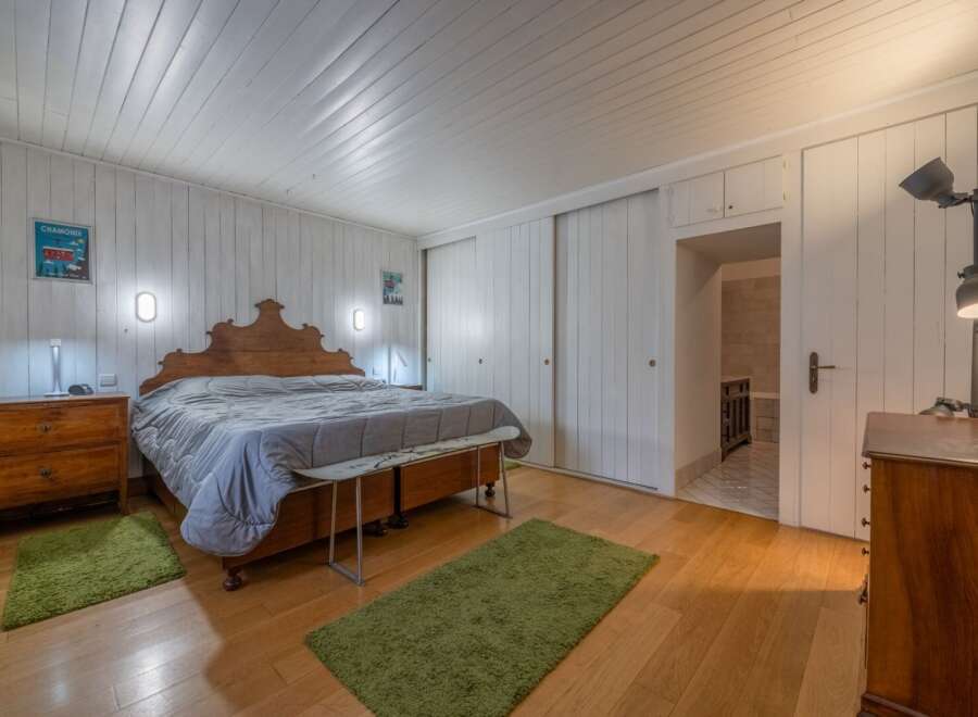 This charming bedroom features a cozy atmosphere with wooden floors and white paneled walls.