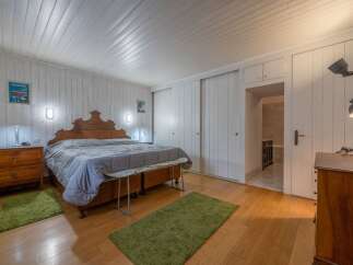 This charming bedroom features a cozy atmosphere with wooden floors and white paneled walls.