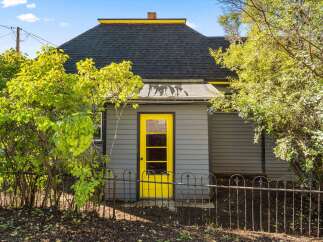 Charming home with a vibrant yellow door and a welcoming wrought iron fence.