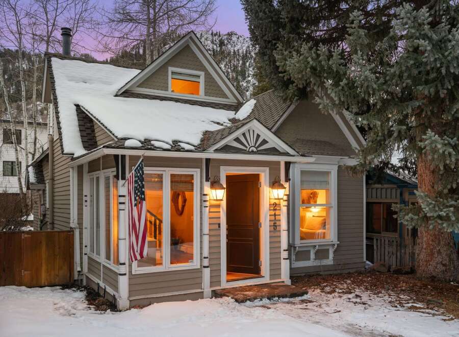 Charming cottage nestled in a winter wonderland, this property boasts a cozy ambiance with its warm interior lighting and inviting facade.