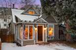 Charming cottage nestled in a winter wonderland, this property boasts a cozy ambiance with its warm interior lighting and inviting facade.