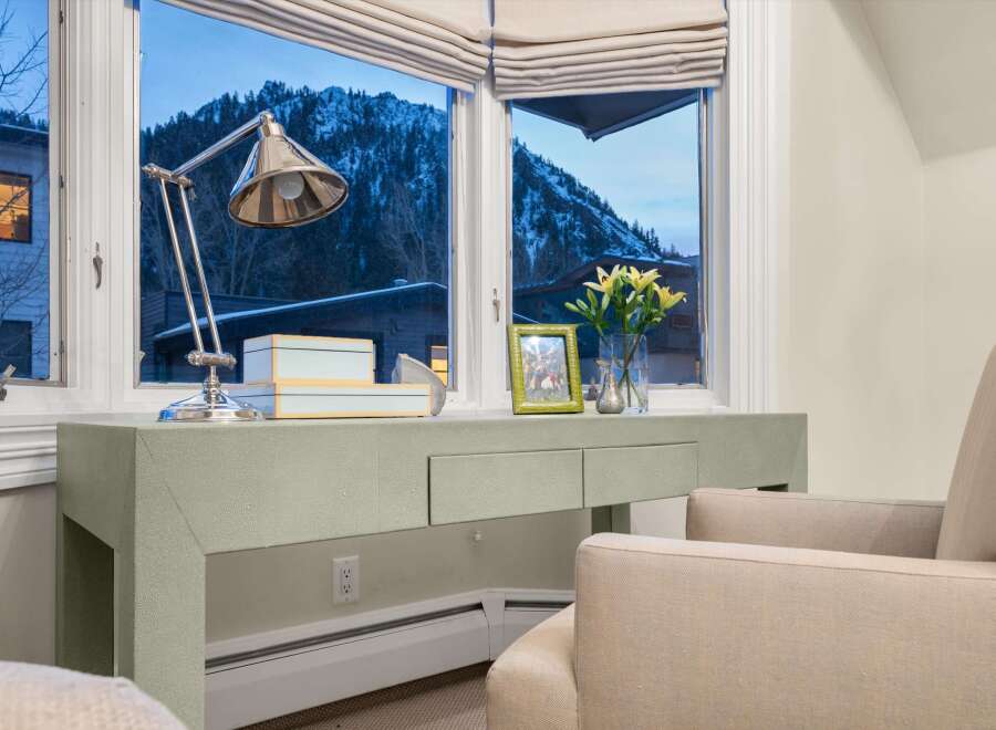 This stunning property boasts a serene interior with a desk area perfectly positioned by a window, offering breathtaking views of a snow-covered mountain.
