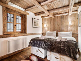 Experience rustic charm in this cozy bedroom featuring exposed wooden beams and a charming window overlooking a snowy landscape.