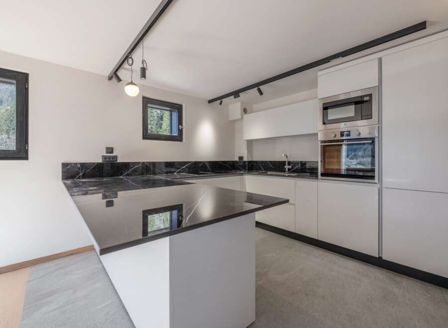 This modern kitchen boasts sleek, white cabinetry and a stunning black marble countertop, creating a sophisticated and stylish space.