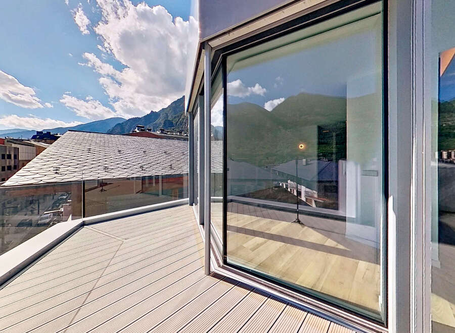 Experience breathtaking views from this modern property featuring a spacious balcony with a sleek glass railing.