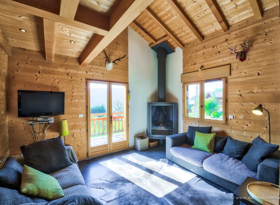 Cozy chalet living room with wood-paneled walls, a fireplace, and large windows offering scenic views.