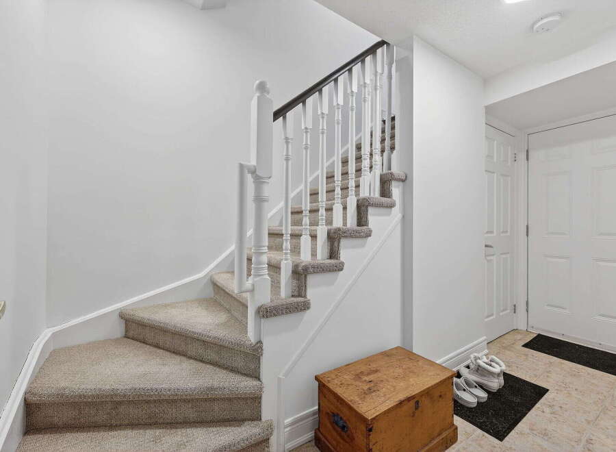 This inviting entryway features a beautiful staircase with carpeted steps and a classic white railing.