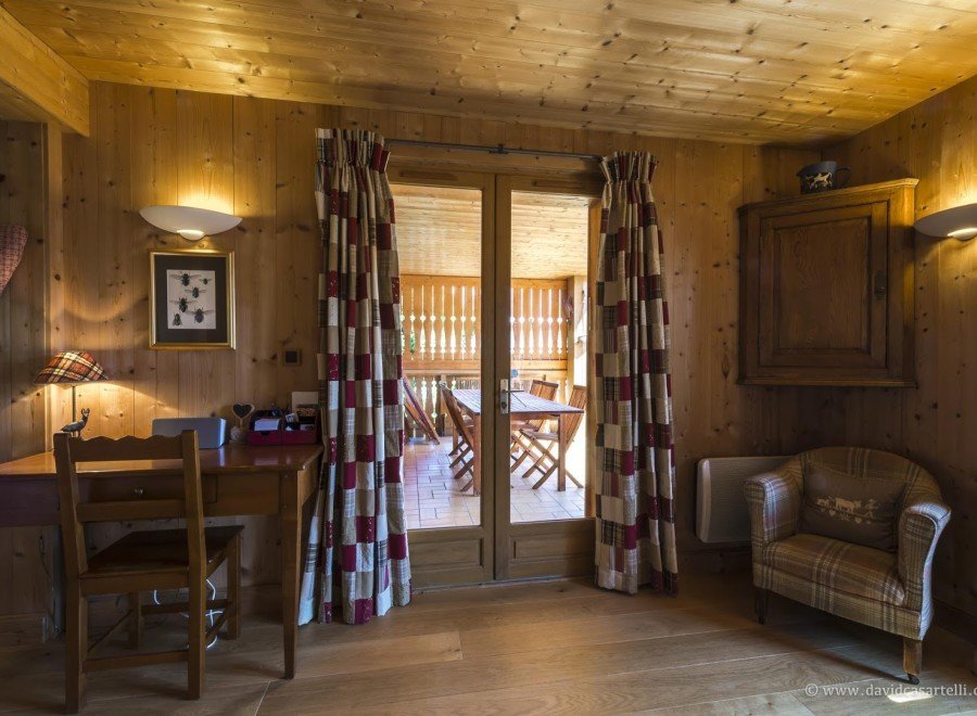 Cozy chalet with wooden interior, featuring a quaint workspace and a relaxing armchair by the patio doors.
