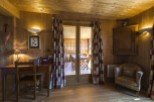 Cozy chalet with wooden interior, featuring a quaint workspace and a relaxing armchair by the patio doors.