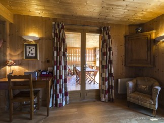 Cozy chalet with wooden interior, featuring a quaint workspace and a relaxing armchair by the patio doors.