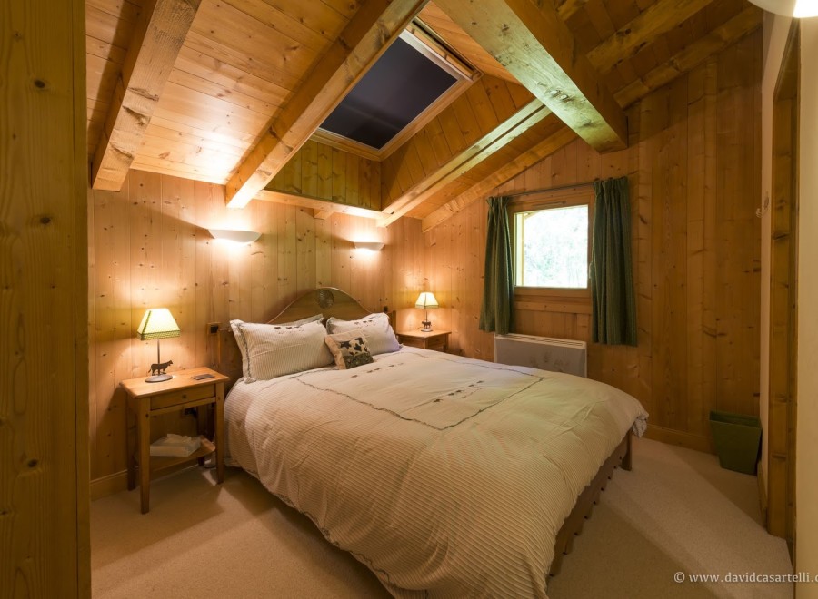 Cozy chalet bedroom with wooden walls and ceiling, featuring a comfortable double bed and skylights.