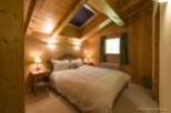 Cozy chalet bedroom with wooden walls and ceiling, featuring a comfortable double bed and skylights.