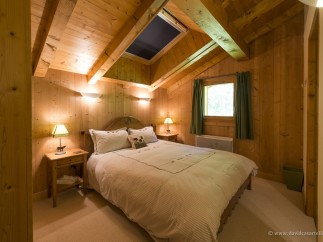 Cozy chalet bedroom with wooden walls and ceiling, featuring a comfortable double bed and skylights.