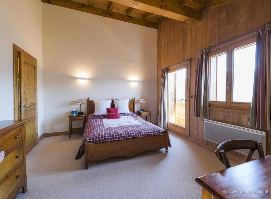 Cozy chalet bedroom with wooden beams, plaid bedding, and stunning mountain views.