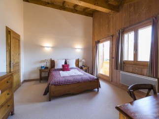 Cozy chalet bedroom with wooden beams, plaid bedding, and stunning mountain views.