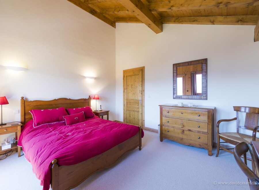 This charming bedroom features a wooden bed frame with a red duvet, wooden nightstands with lamps, and a dresser with a mirror.