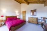 This charming bedroom features a wooden bed frame with a red duvet, wooden nightstands with lamps, and a dresser with a mirror.