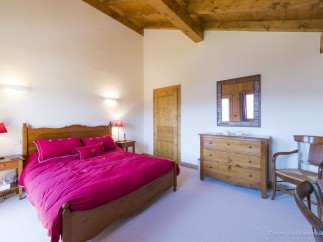 This charming bedroom features a wooden bed frame with a red duvet, wooden nightstands with lamps, and a dresser with a mirror.
