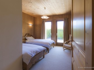 Cozy chalet bedroom with twin beds, wooden walls, and access to a private garden.
