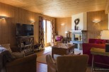 Cozy chalet living room with wooden walls and beamed ceiling, featuring a fireplace, comfortable leather armchairs, and a large flat-screen TV.