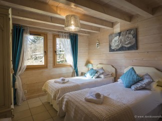 Charming twin bedroom with wooden walls and beams, featuring teal accents and white bedding.