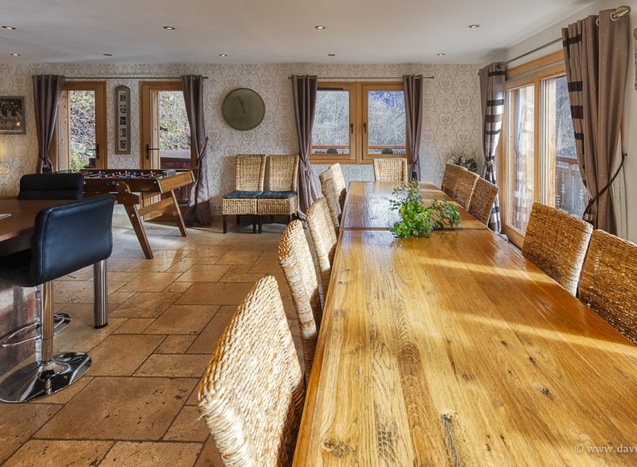 This stunning property boasts a spacious dining area with a long wooden table perfect for gatherings, complemented by comfortable wicker chairs.