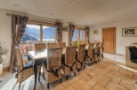 This stunning chalet boasts a spacious dining area with a large table perfect for family gatherings, surrounded by wicker chairs and offering breathtaking mountain views through expansive windows.