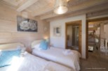 Cozy chalet bedroom with twin beds, featuring a rustic wood interior and soft, elegant decor.
