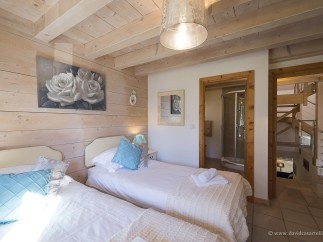 Cozy chalet bedroom with twin beds, featuring a rustic wood interior and soft, elegant decor.
