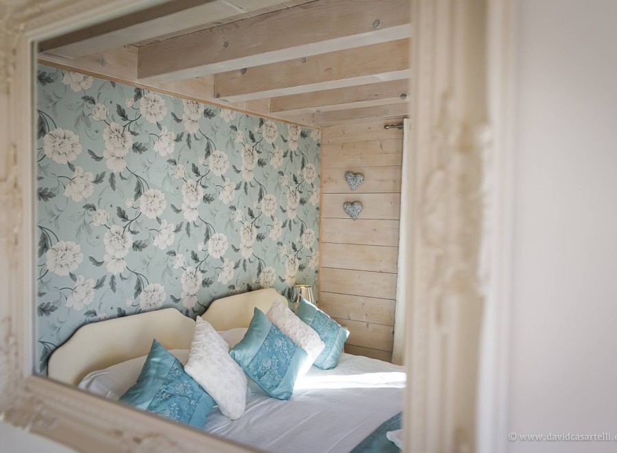 Romantic bedroom with floral wallpaper and light wood walls.