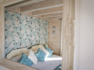Romantic bedroom with floral wallpaper and light wood walls.