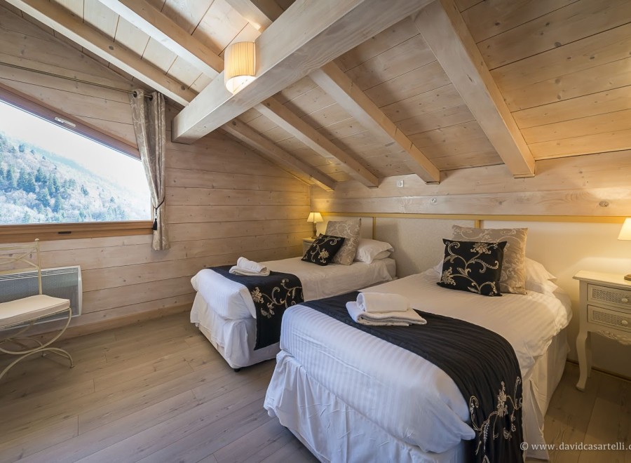 Cozy chalet bedroom with twin beds, featuring a stunning mountain view from a large window.