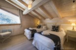 Cozy chalet bedroom with twin beds, featuring a stunning mountain view from a large window.