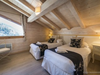 Cozy chalet bedroom with twin beds, featuring a stunning mountain view from a large window.