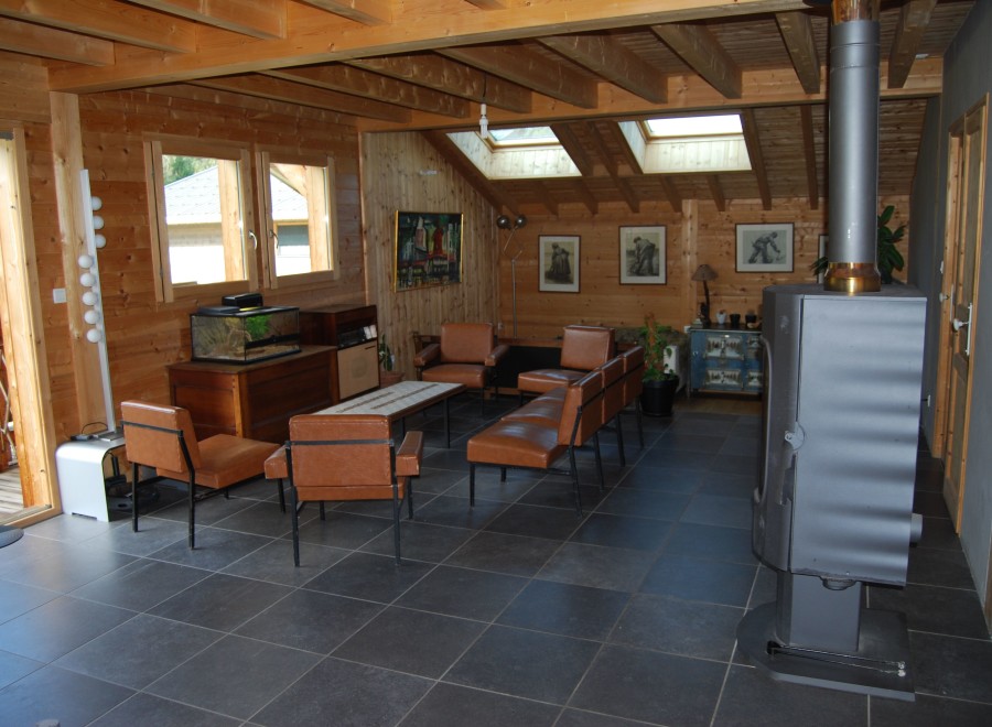Cozy chalet living room with wood-beamed ceiling, large windows, and a wood-burning stove.