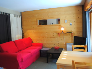 Cozy living room with red couch and wood wall.