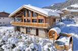 This stunning chalet boasts a beautiful wooden design and is nestled in a snowy mountain landscape.