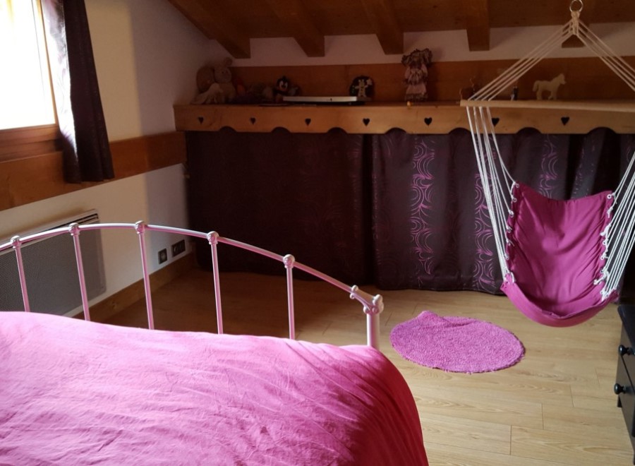 Charming attic bedroom with a comfy pink bed and a hanging chair, perfect for relaxing.
