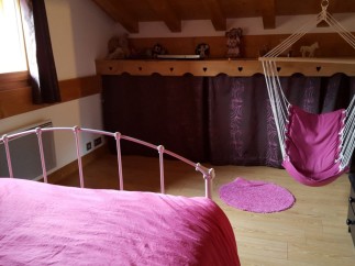 Charming attic bedroom with a comfy pink bed and a hanging chair, perfect for relaxing.