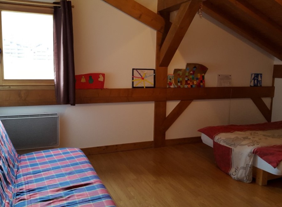 Cozy attic bedroom with wooden beams, featuring a comfortable sofa bed and a single bed, perfect for a relaxing getaway.